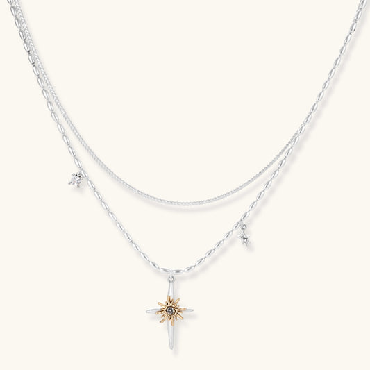 Two-layer silver-toned necklace with star charms and dagger pendant featuring golden sun motif on white background.